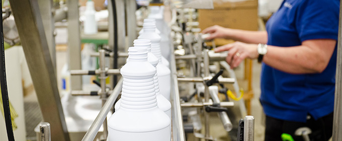 Woman with dark, shoulder length hair, wearing blue polo shirt working on the liquid filling cleaning line.